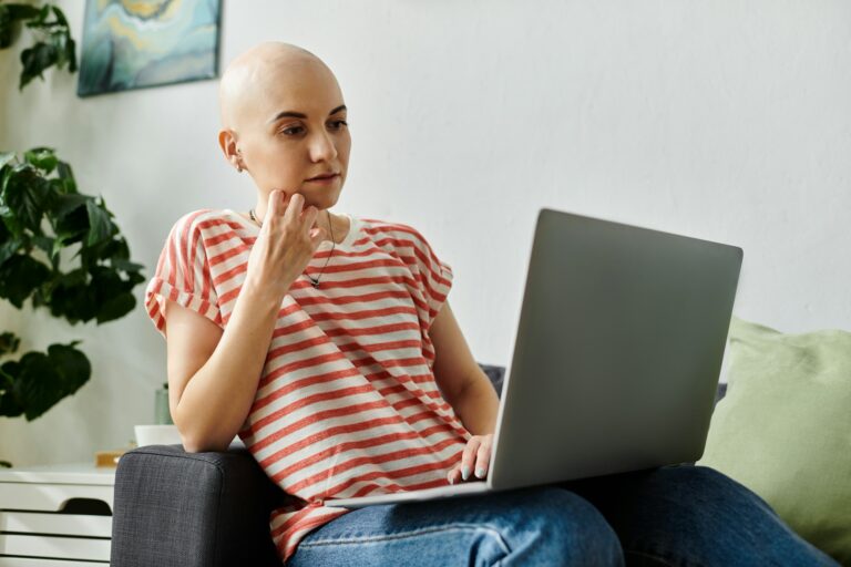 Young bald woman with alopecia focused on her laptop while relaxing at home on a sunny day